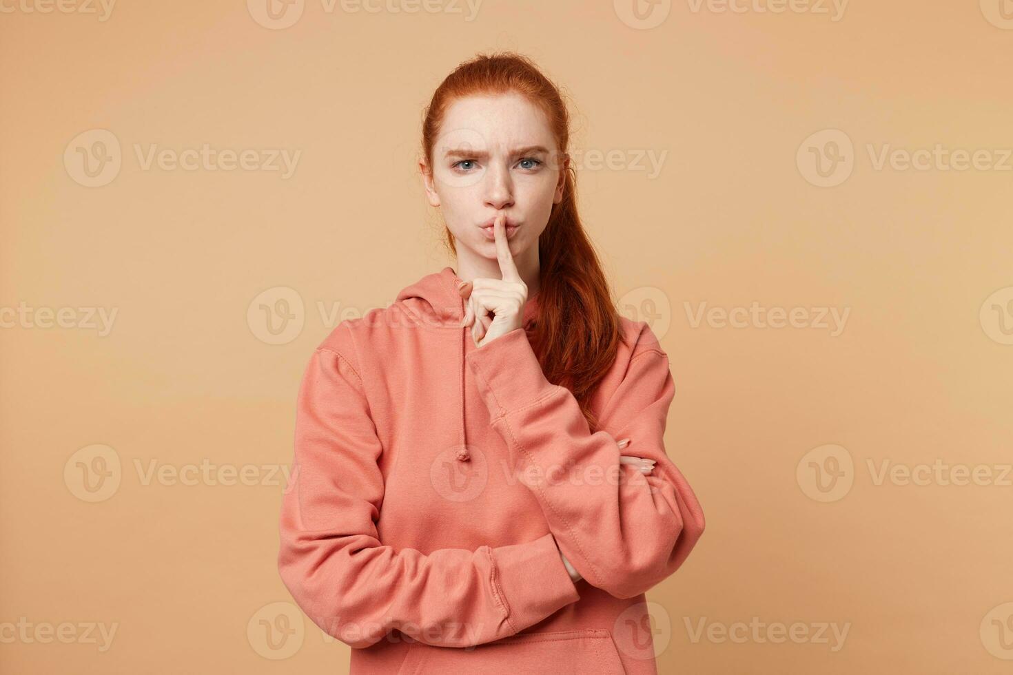 interior foto de Pelirrojo grave niña con un cola con hermosa azul ojos, urge a mantener silencio, a comportarse en silencio, a calma abajo no a Produce ruido, aislado en un beige antecedentes.