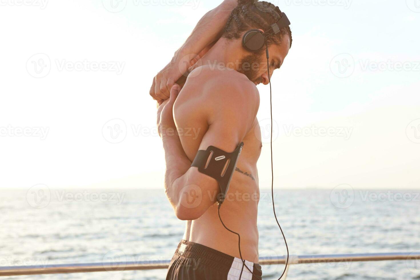 Young sporty handsome bearded guy enjoy the morning , does stretching exercises, has muscular body shape, listen favorite music on headphones. photo