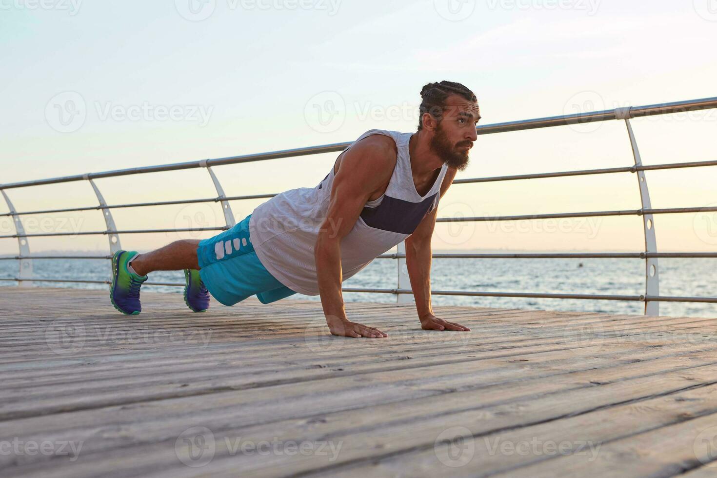 joven masculino deportivo barbado chico haciendo Mañana ejercicios por el mar, calentar después correr, haciendo Lagartijas, mantiene el tablón, Guías sano activo estilo de vida. aptitud masculino modelo. foto