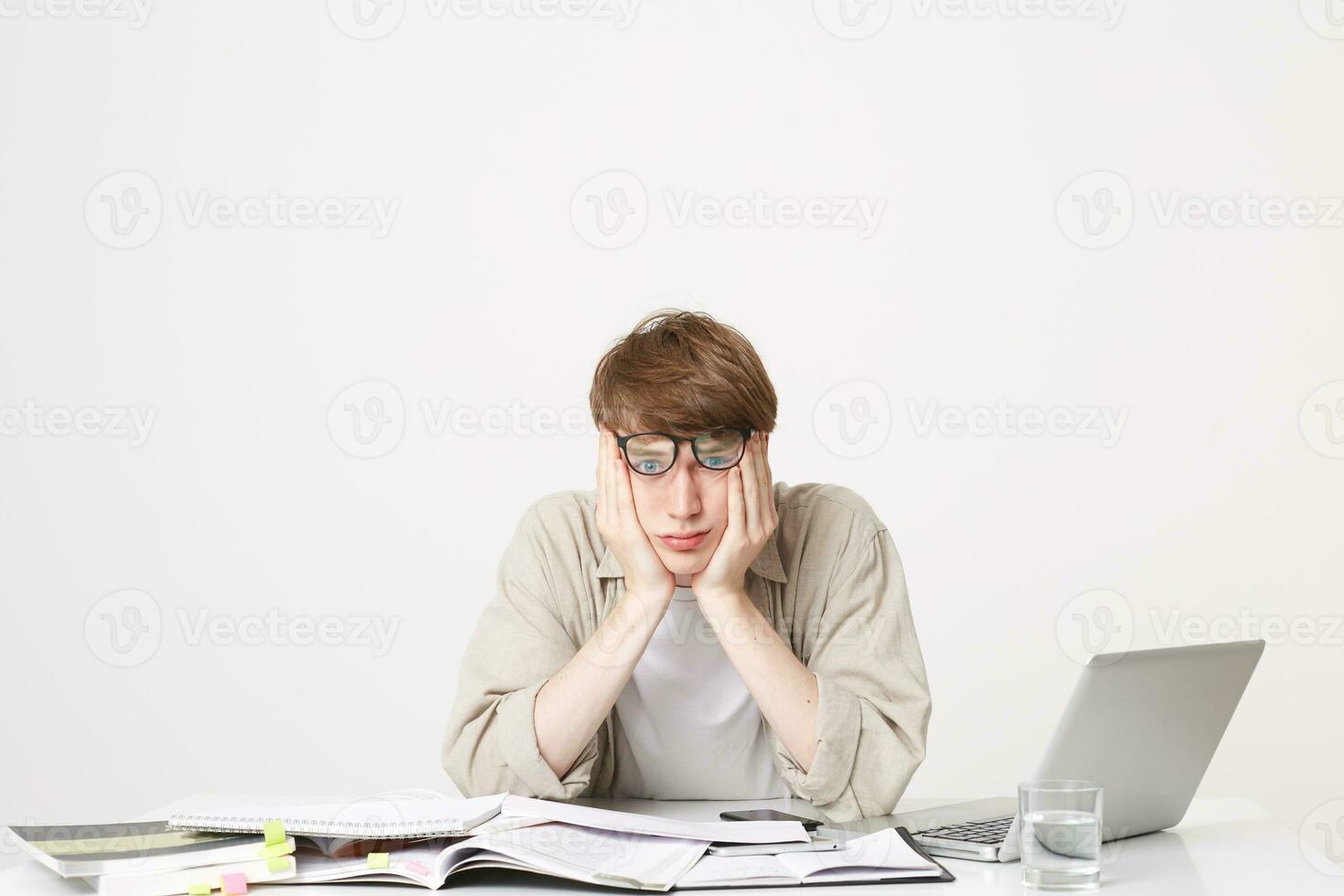 Studio photo of tired student sitting with his elbows on his desk holding his head, looking directly through his glasses, looks a little depressed, weary of many hours of practice