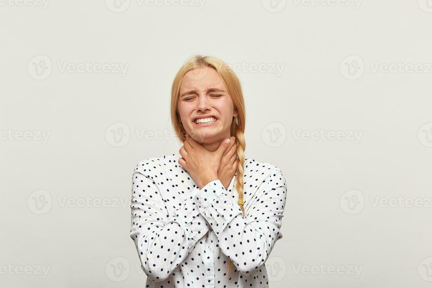 Studio portrait of a blonde young girl with hair gathered in braid frustrated distressed upset, hands strangling herself almost crying. Over white background photo