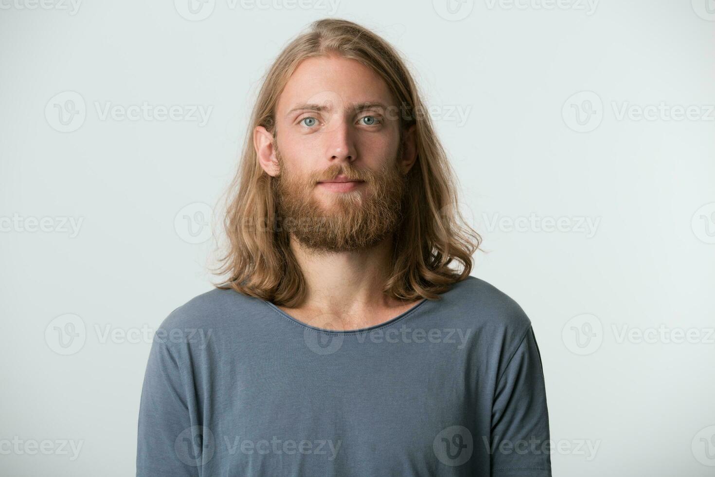 retrato de hermoso barbado joven hombre con rubia largo pelo usa gris t camisa mira grave y confidente aislado terminado blanco antecedentes foto
