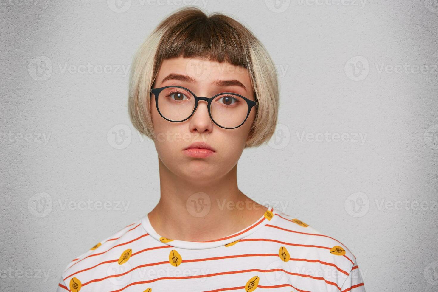 Portrait of upset beautiful young woman wears striped t shirt and glasses feels sad and depressed isolated over white background Looks directly in camera photo