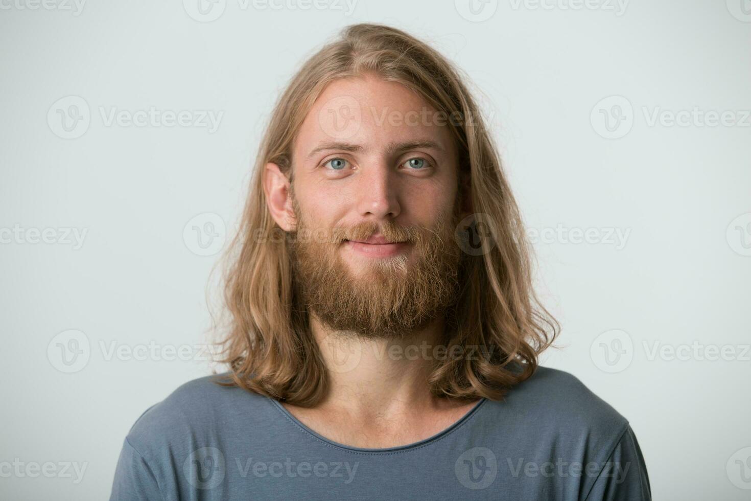 Portrait of smiling handsome bearded young man with blonde long hair wears gray t shirt feels happy and confident isolated over white background photo
