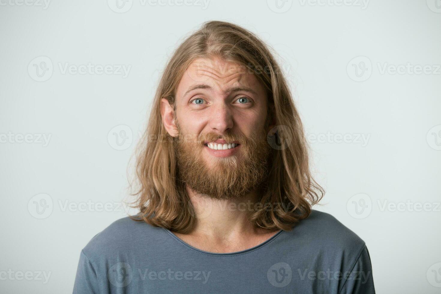 Closeup of confused sad young man with beard and blonde long hair wears gray t shirt feels embarrassed and upset isolated over white background photo