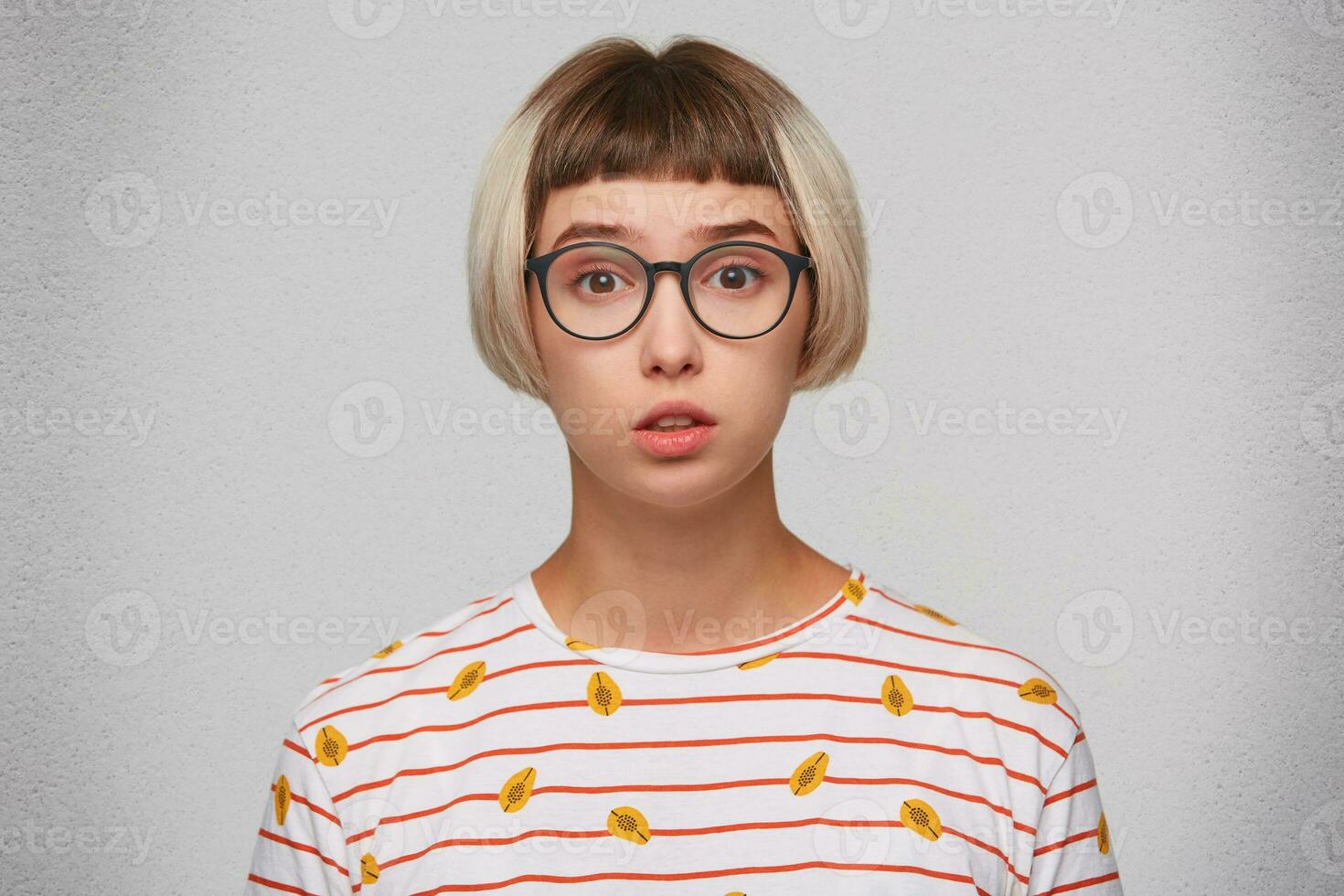 Closeup of unhappy shocked young woman wears striped t shirt and spectacles feels stunned and worried isolated over white background photo