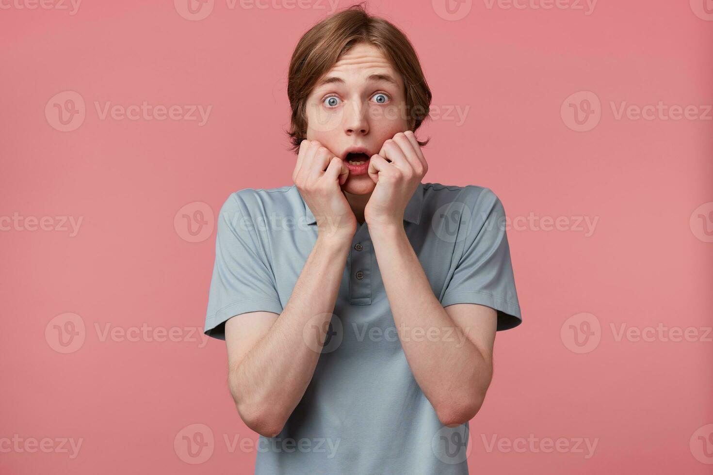 Portrait of scared teen in panic nervous excited mouth opened in fear dressed in polo t-shirt keeps palm on face, feels himself frightened, isolated on pink background with copy space photo
