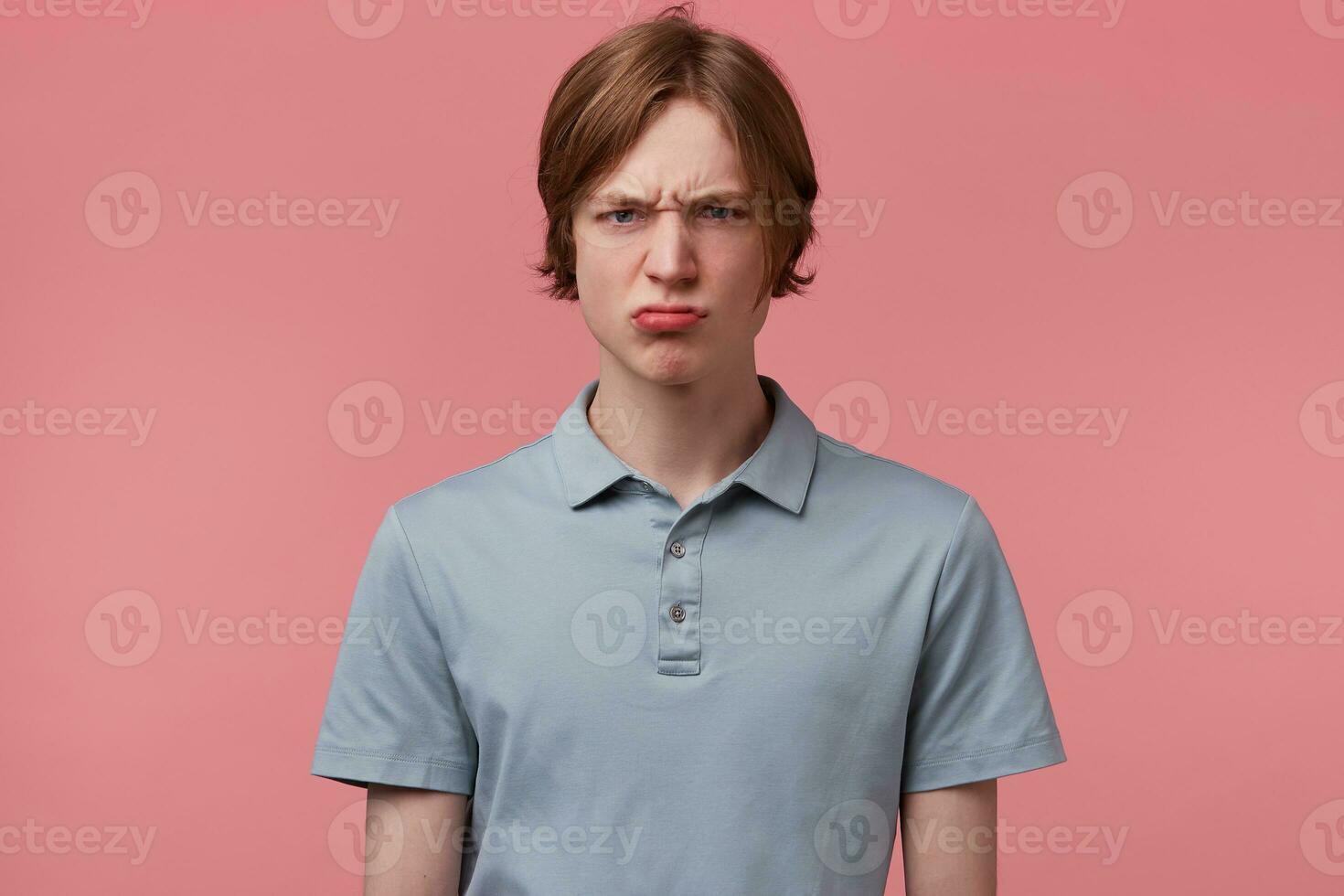 Dissatisfied neatly combed young guy, eyebrows frowned, eyes aggressive angry, dressed in casual polo T-shirt, isolated over pink background photo