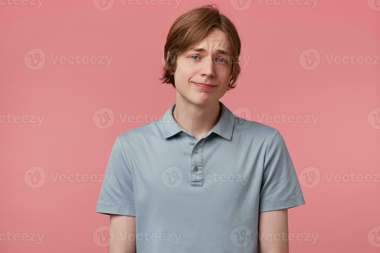 Cheerful pleased european guy with blue eyes neatly combed looks carefree optimistic dressed in elegant T-shirt in good mood while posing in studio against pink background. Facial expressions concept photo