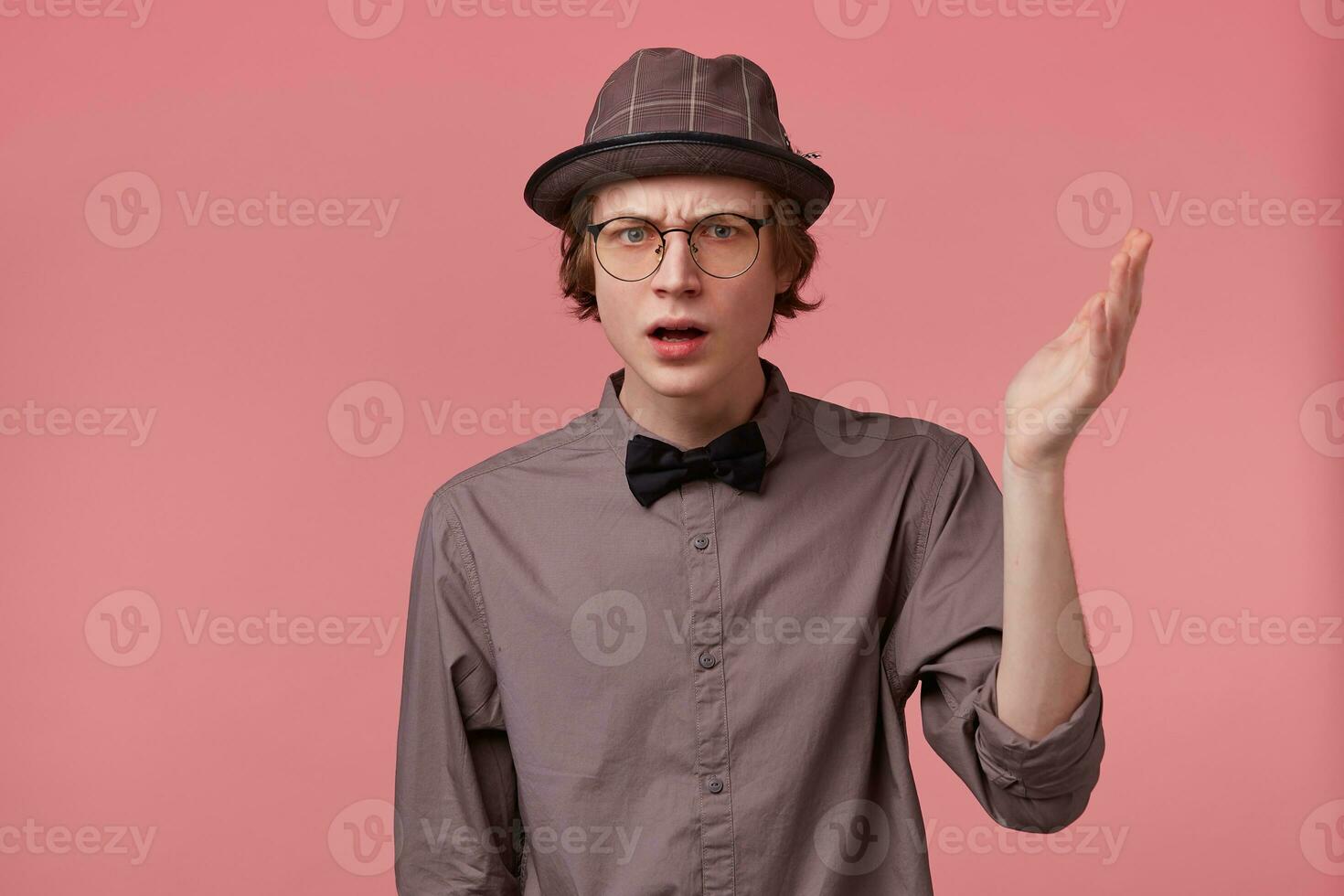 Unsatisfied serious young smartly dressed guy holding hand up looking camera through glasses moralizing, defends his point of view, makes moral lecture, over pink background photo