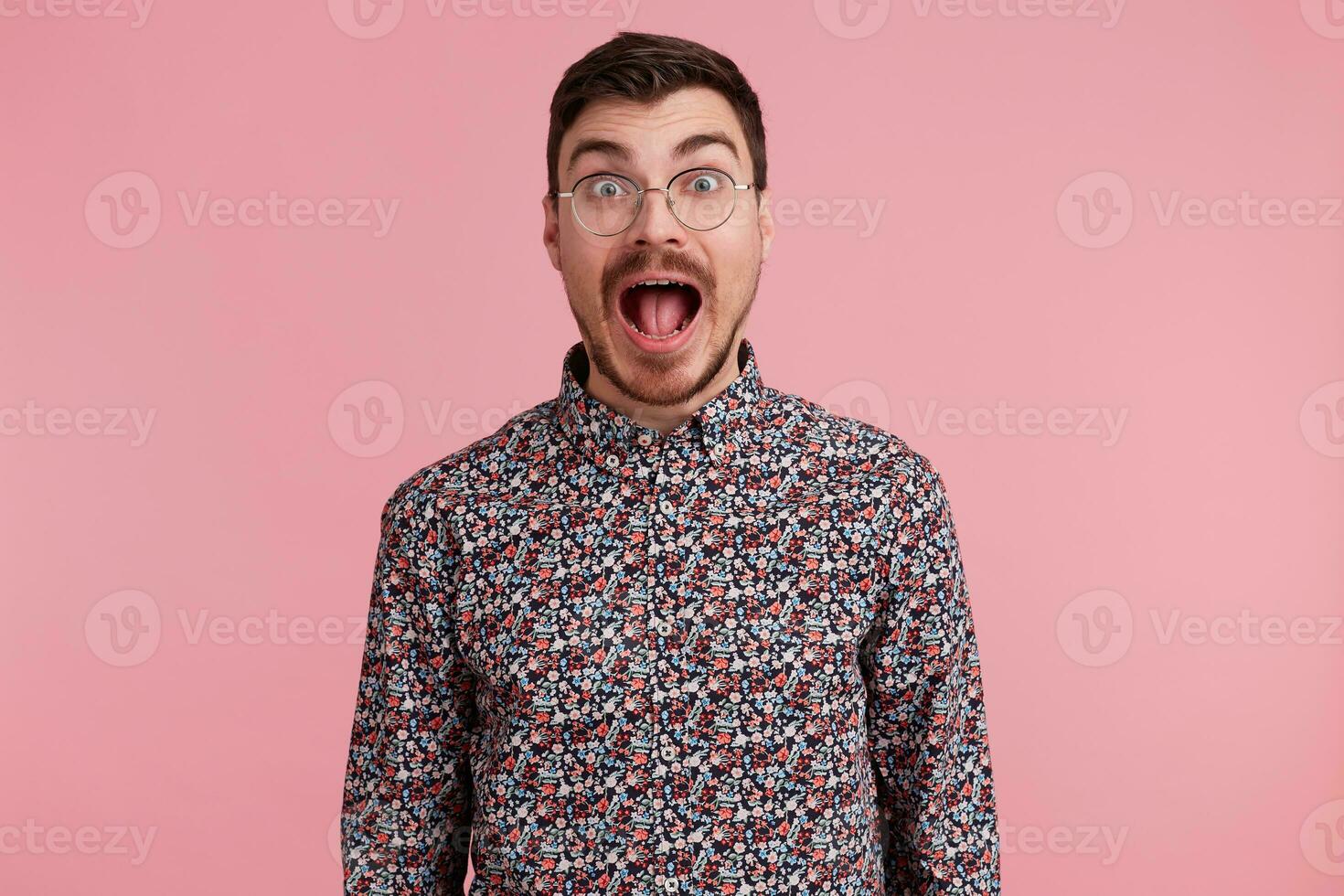 Frightened man popping eyes and shouts loudly. Surprised male, keeps mouth open, being stunned, over pink background. Horizontal shot of shocked young male, expresses panic, catastrophe had happened photo