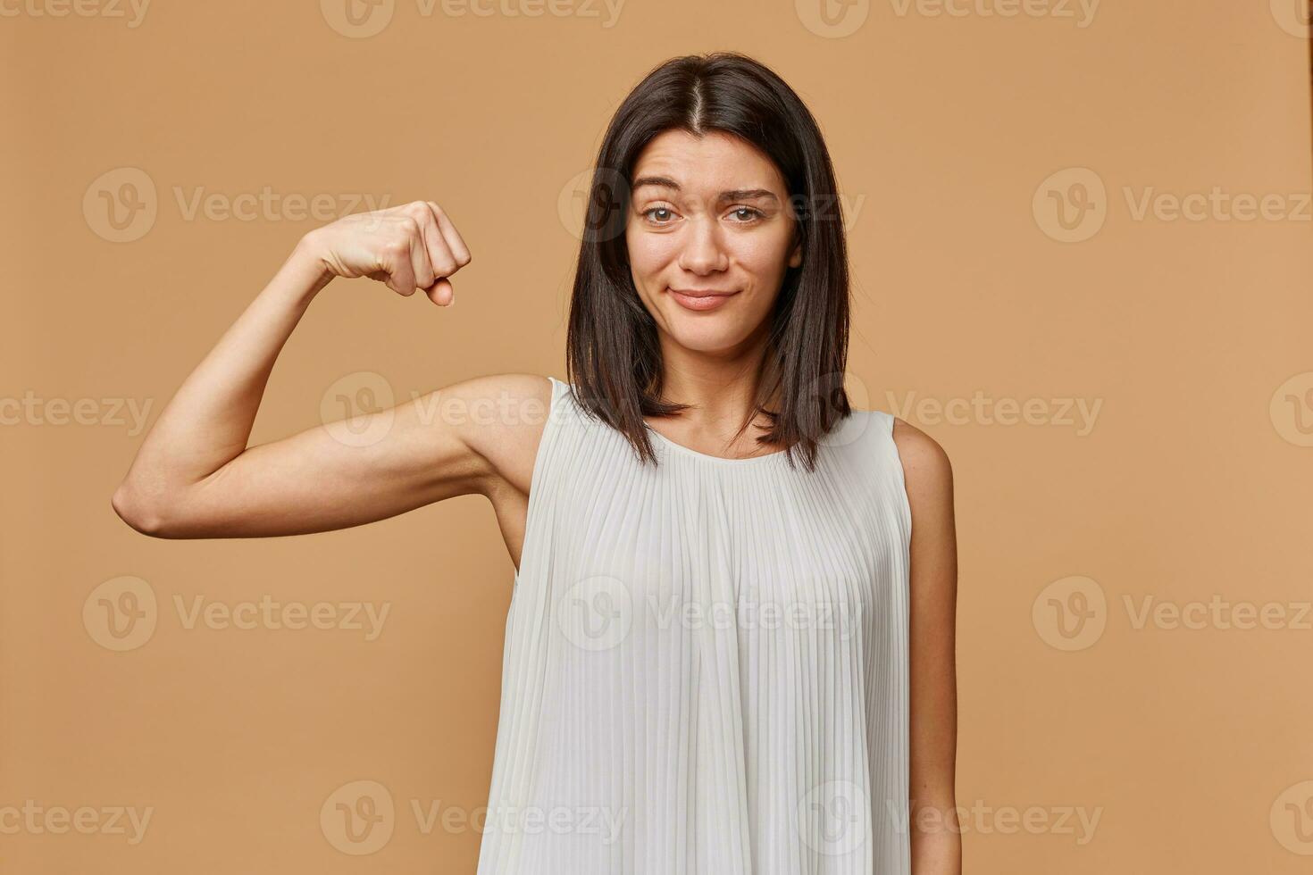 Portrait of a girl confident proud of her strength clenches a fist and bent her arm to show her muscles, isolated over beige background photo
