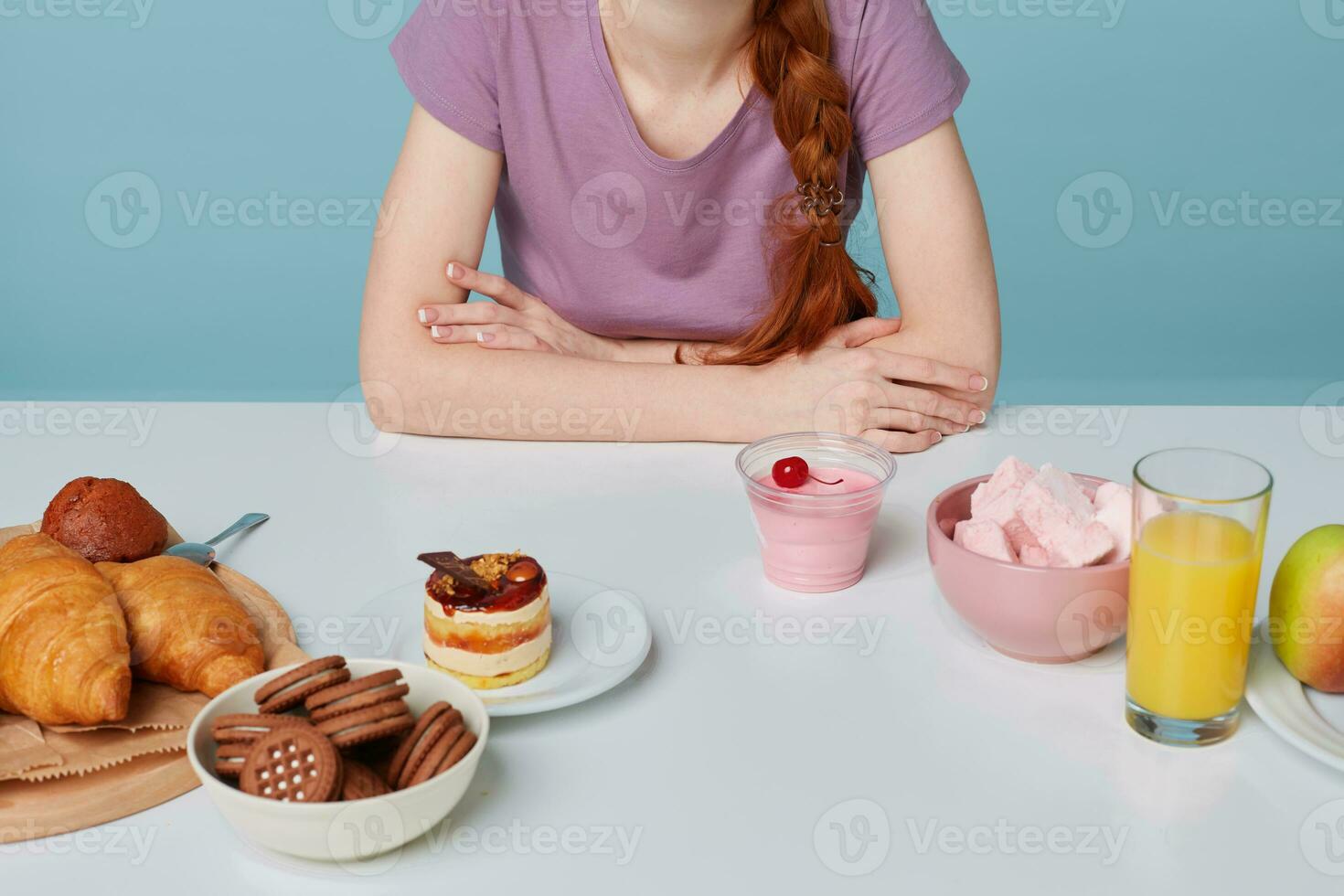 Close up flat lay of a white kitchen table where lay baking and fresh fruit juice cherry yogurt, women's hands are crossed on a table, isolated on a blue background. Concept of choice, diet, food. photo