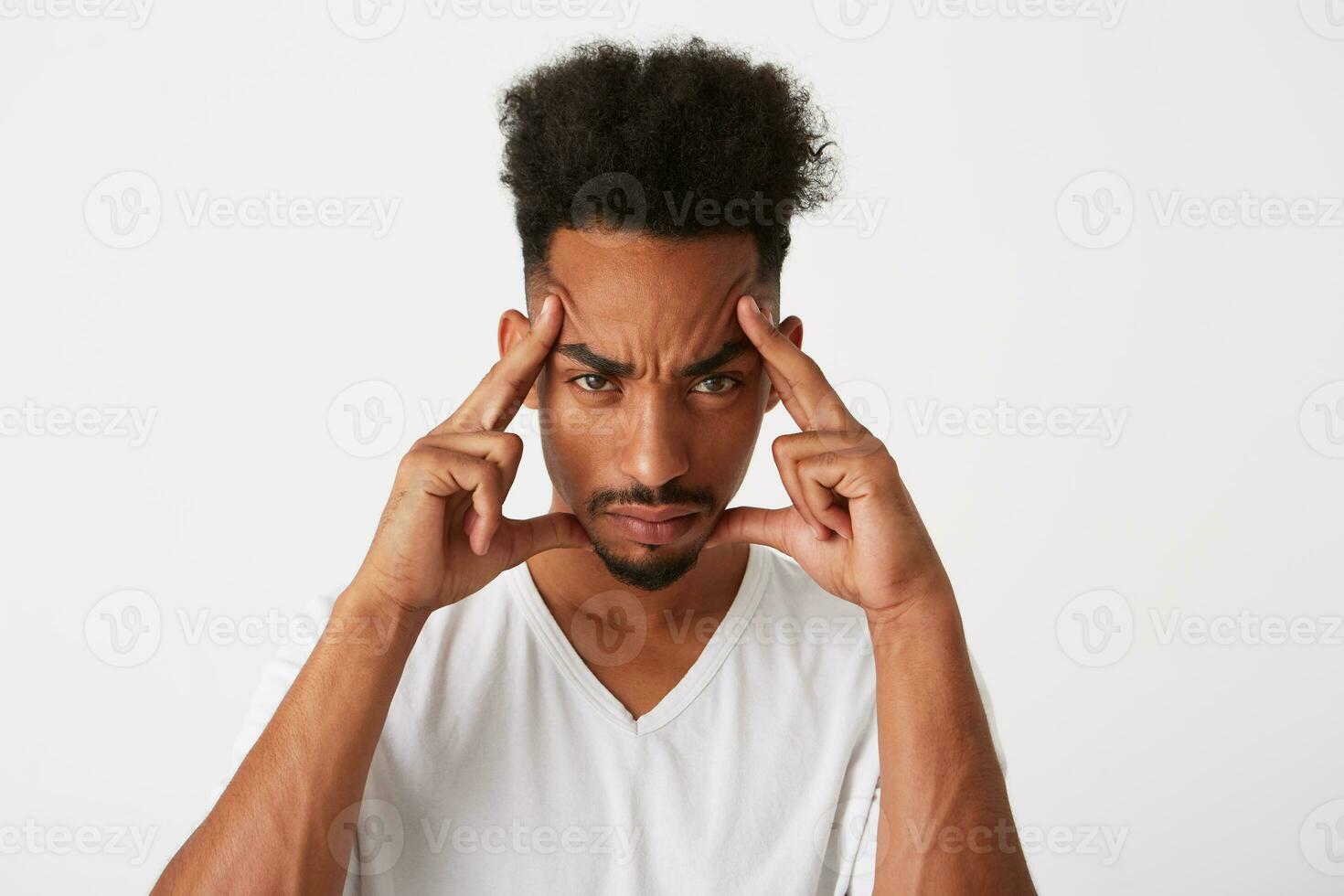 Portrait of unhappy thoughtful african american young man with curly hair wears t shirt thinking, touching his temples and having headache isolated over white background photo