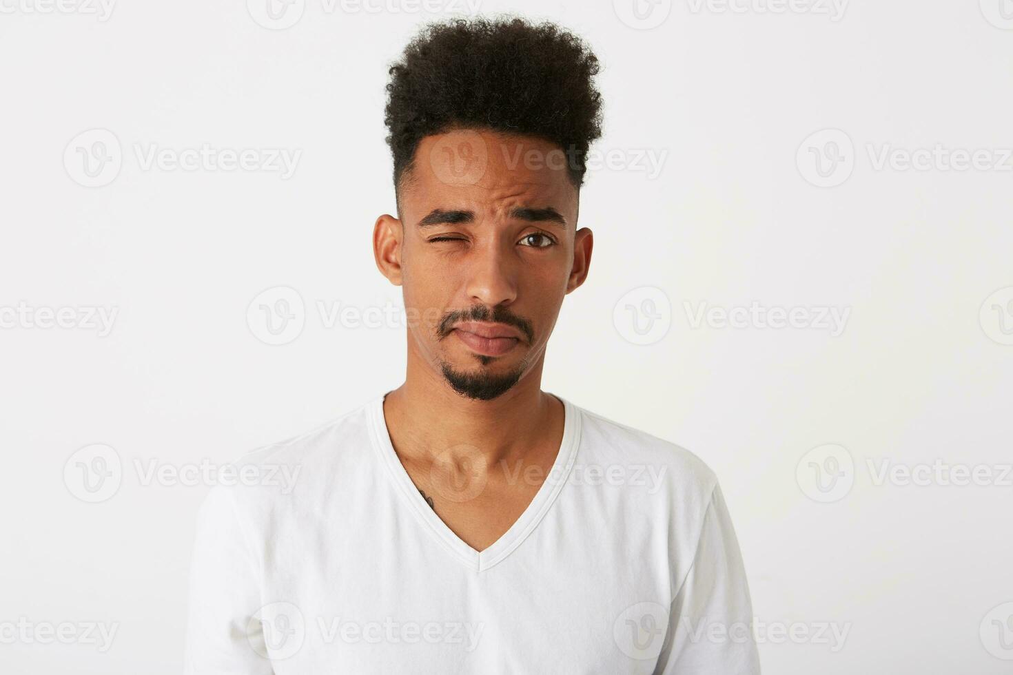 Closeup of playful handsome african american young man with curly hair wears t shirt looks serious and winking isolated over white background photo