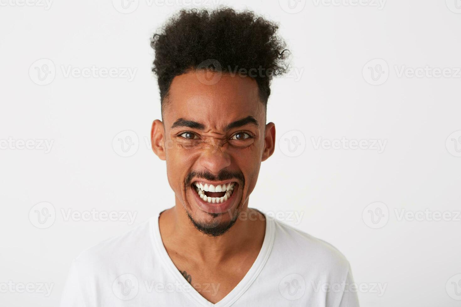 Closeup of mad furious african american young man with curly hair wears t shirt looks crazy and screaming isolated over white background photo