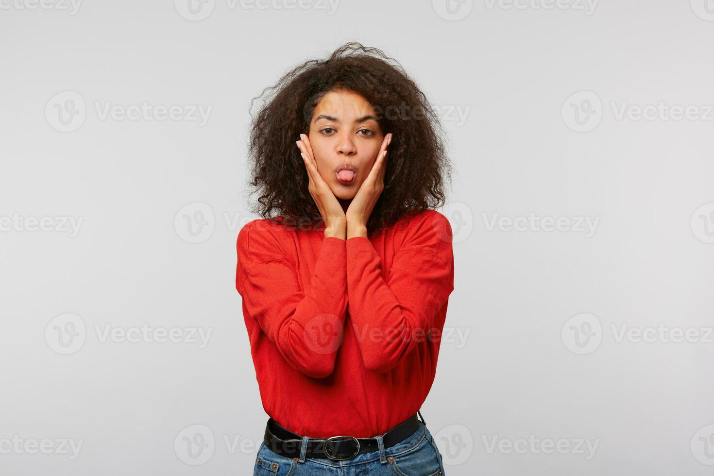 bonito africano americano niña hermosa mujer, joven, linda en rojo manga larga con largo afro peinado muestra lengua conmovedor cara con palmas en blanco antecedentes foto