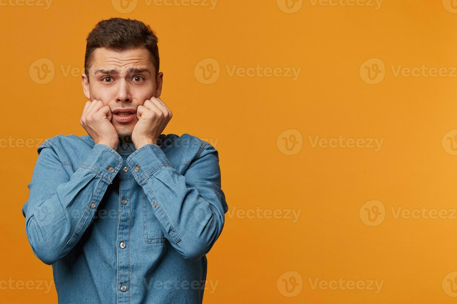 Headshot of hysterical student guy looking in despair and panic, nervous, worried about the exam results, keeps fists near his face,isolated over yellow background, with copy space for your text photo