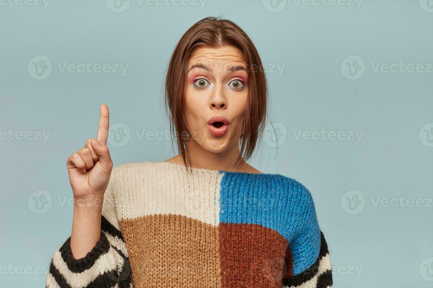 Young girl in checkered sweater and a bright make-up came up with a great idea Model woman inspired excited isolated on bright blue background photo