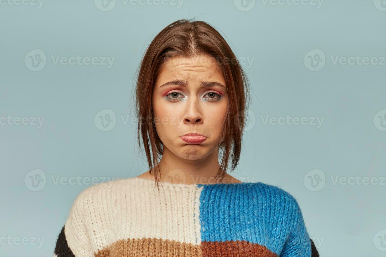 Headshot of emotional woman with a sad expression on face, crooked lower lip with a disgruntled look. The girl received bad words about her work, feels disappointed, isolated over blue background photo