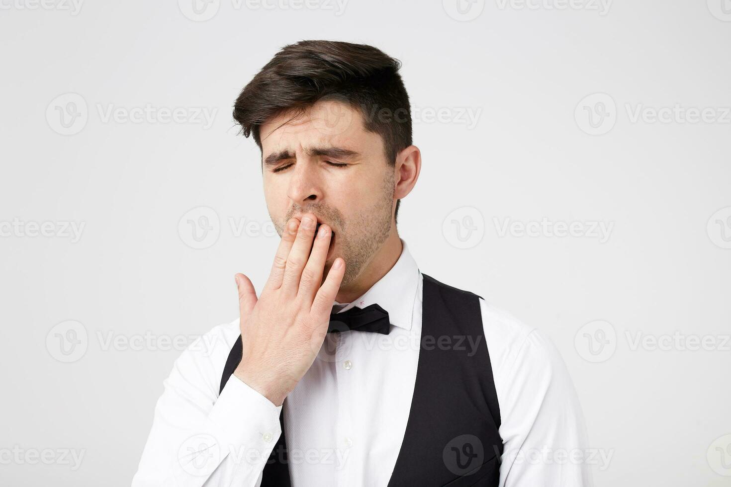 Cute attractive brunette in a suit danced all night, now tired yawns cover his mouth with his hand, feels drowsiness, is going to go home after party. photo