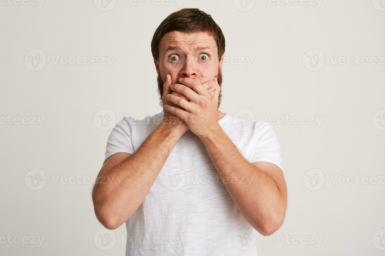 Portrait of shocked amazed young man with beard wears t shirt looks astonished photo