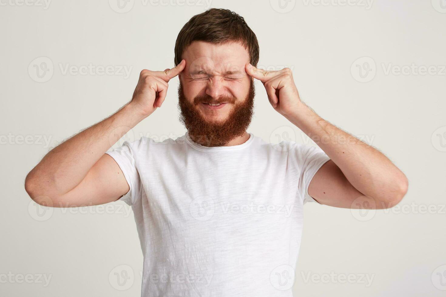 Closeup of stressed tensed young man with beard wears t shirt touching temples photo