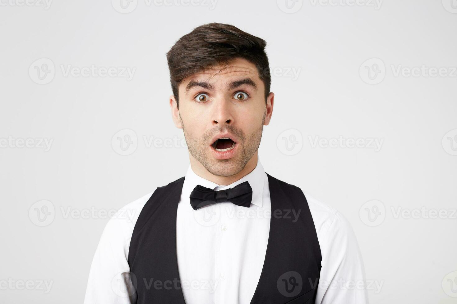 The brunette, neatly dressed in a white shirt, vest, black bow tie, looks shocked. Young waiter warmed did not expect to see so many visitors in the hall, get a very small first salary. photo