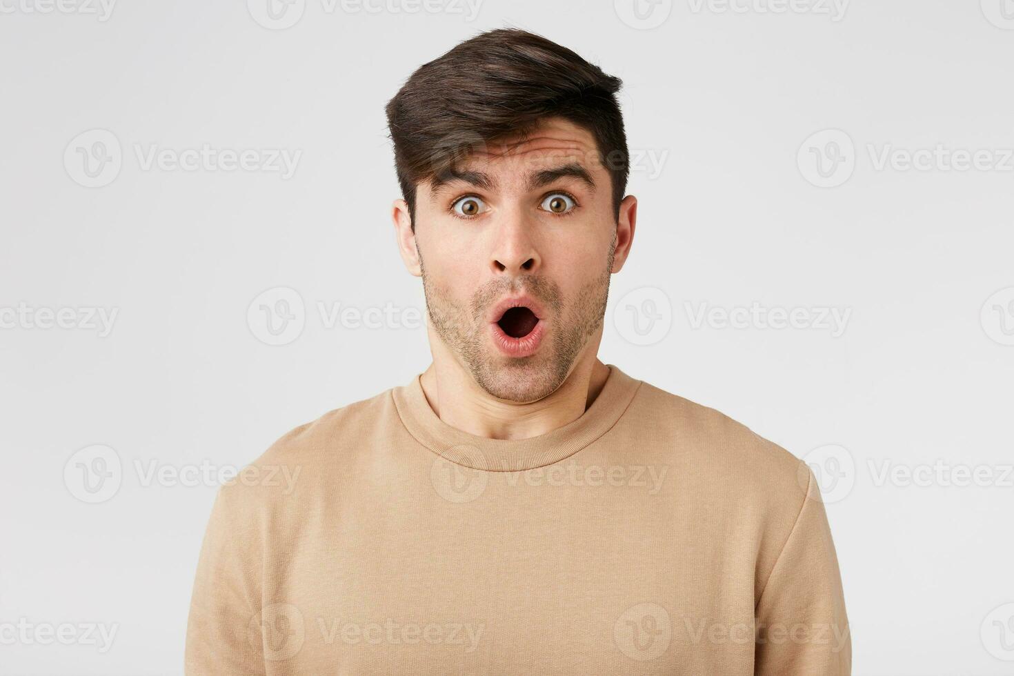 Attractive brunetl looks shocked with open mouth looking at the camera wears flesh-colored sweater, isolated on white background photo