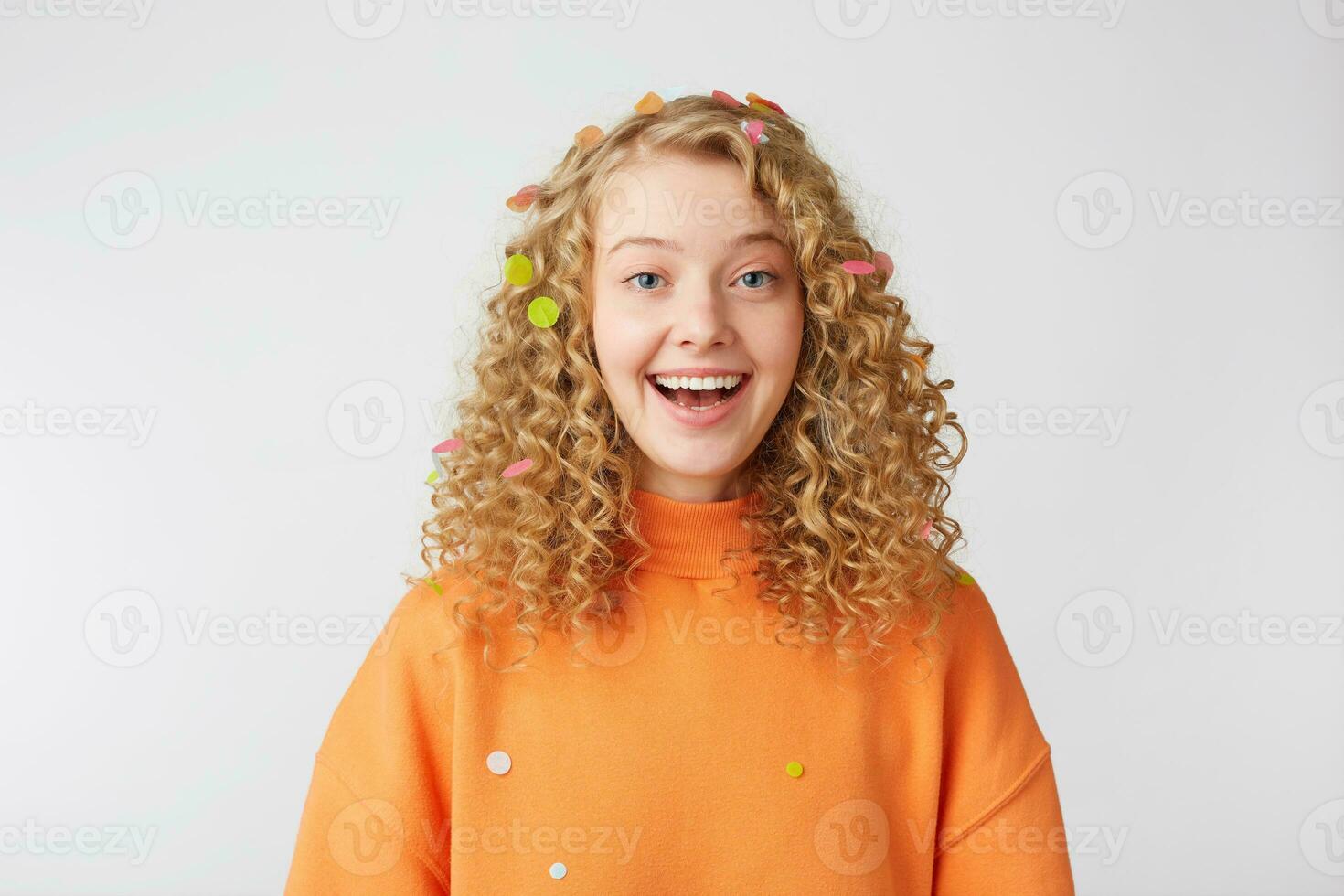 celebrando felicidad, joven mujer con grande sonrisa soportes aislado terminado blanco fondo.rizado rubia en naranja suéter sonrisas disfrutando vida momento, llegó a el día festivo. foto