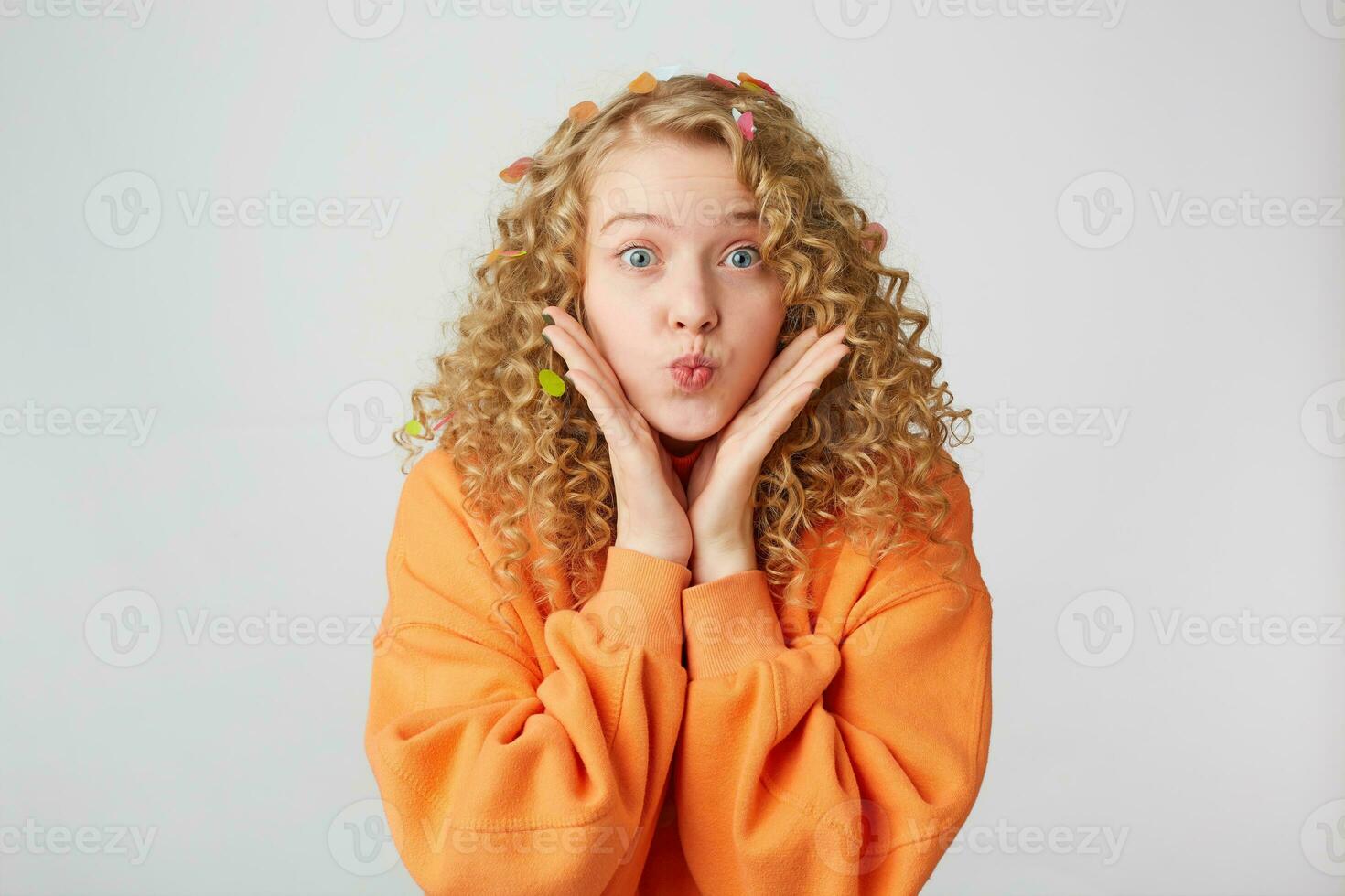 Lovely tender nice girl blows air kiss, keeps palms near face as if demonstrates it or tries to pay attention, dressed in oversized sweatshirt. People, body language and facial expressions concept photo