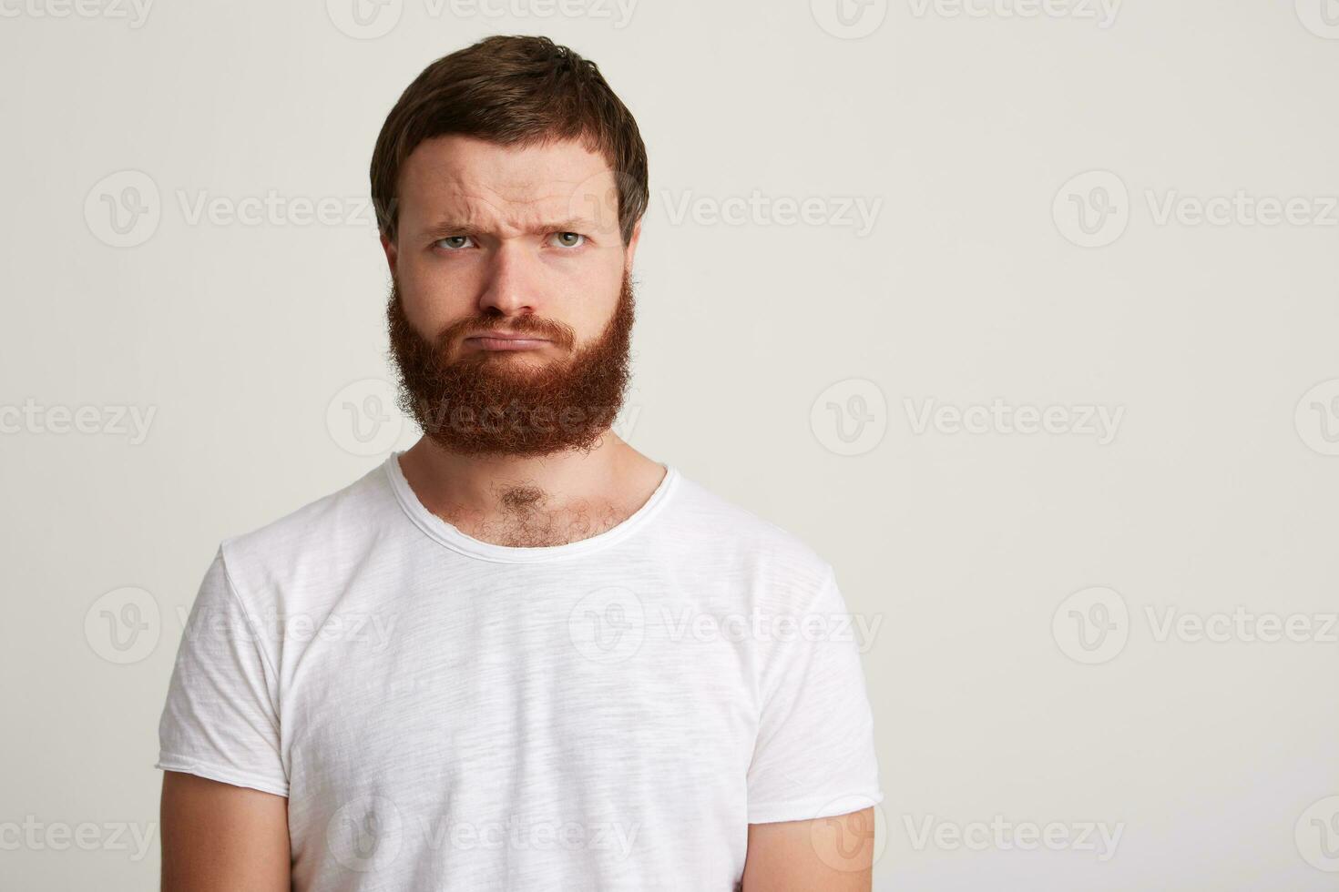 Portrait of sad upset young man hipster with beard wears t shirt feels displeased and depressed isolated over white background Thinking about his problems photo
