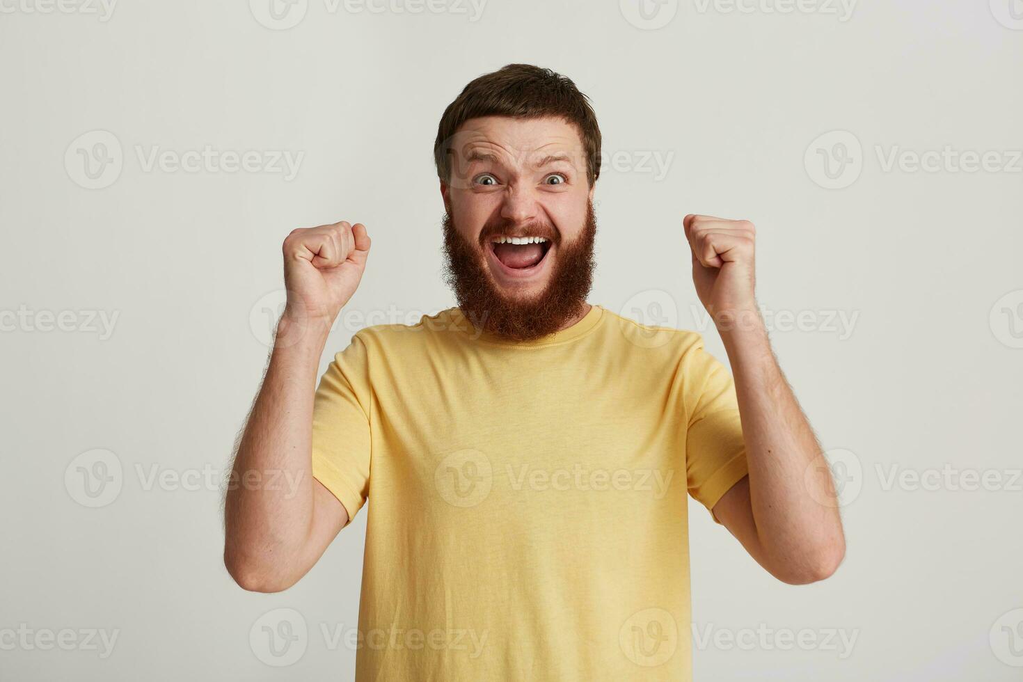 Portrait of cheerful excited young man hipster with beard wears yellow t shirt looks happy, shouting and having fun isolated over white background photo