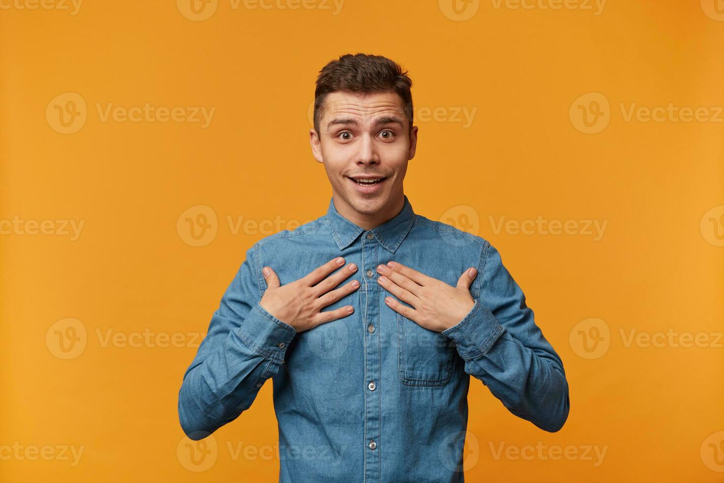 You meen me Photo of delighted by sudden news, overwhelmed with positive emotions, shocked, pleasantly surprised guy in a denim shirt, feels himself as chosen one,can't believe in his luck