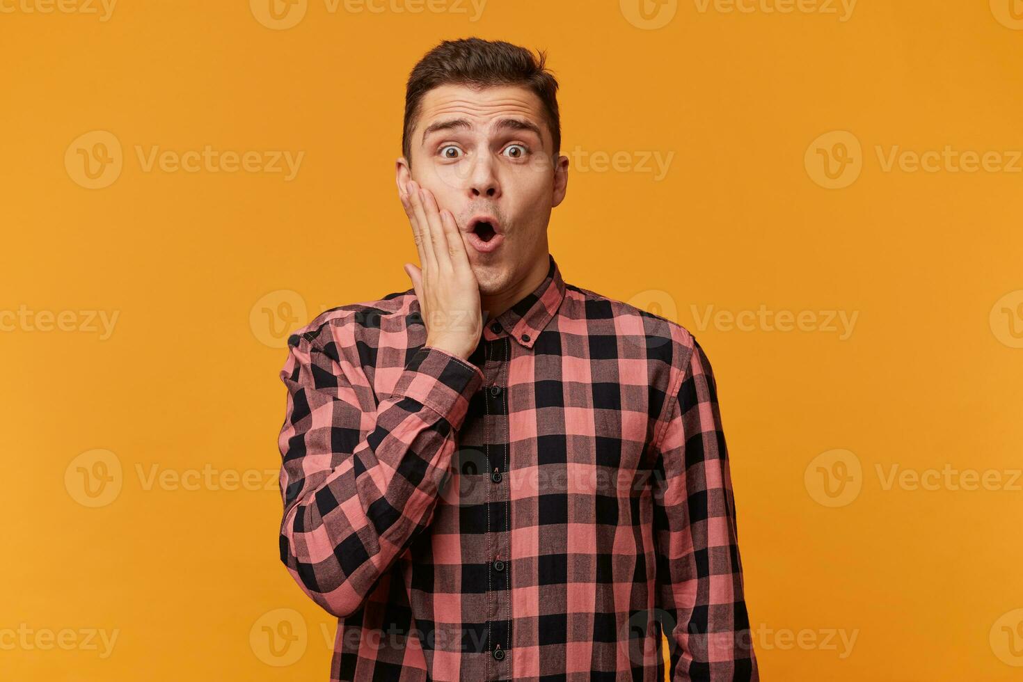 Photo of stunned attractive guy looks with unexpected expression directly at camera, being shocked to recieve increadable news, isolated over yellow background. People, emotions, reaction