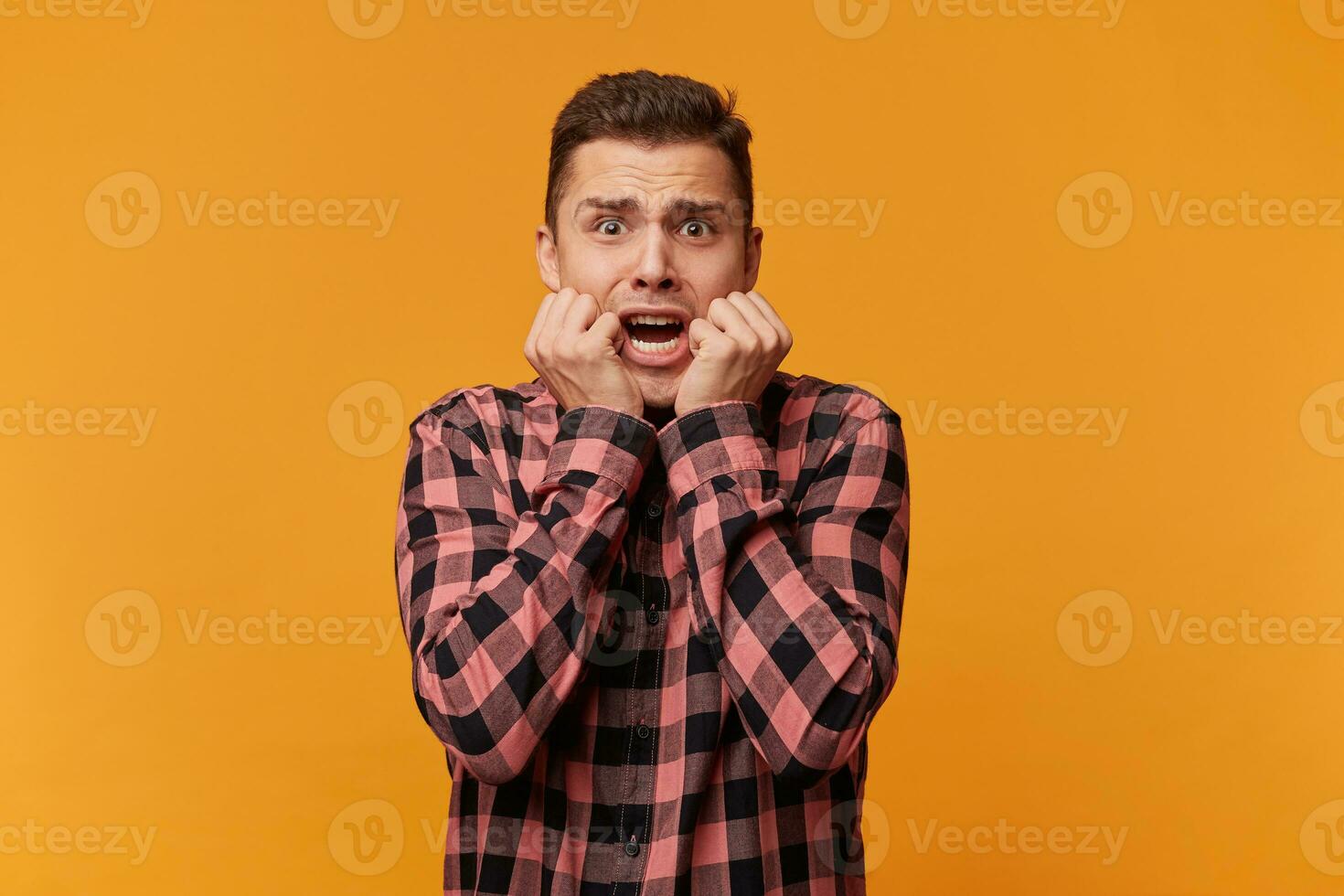 Portrait of hysterical student guy looking in despair and panic, nervous on test, worried about the exam results, not knowing what to answer, hands near mouth, mouth opened in a shout photo