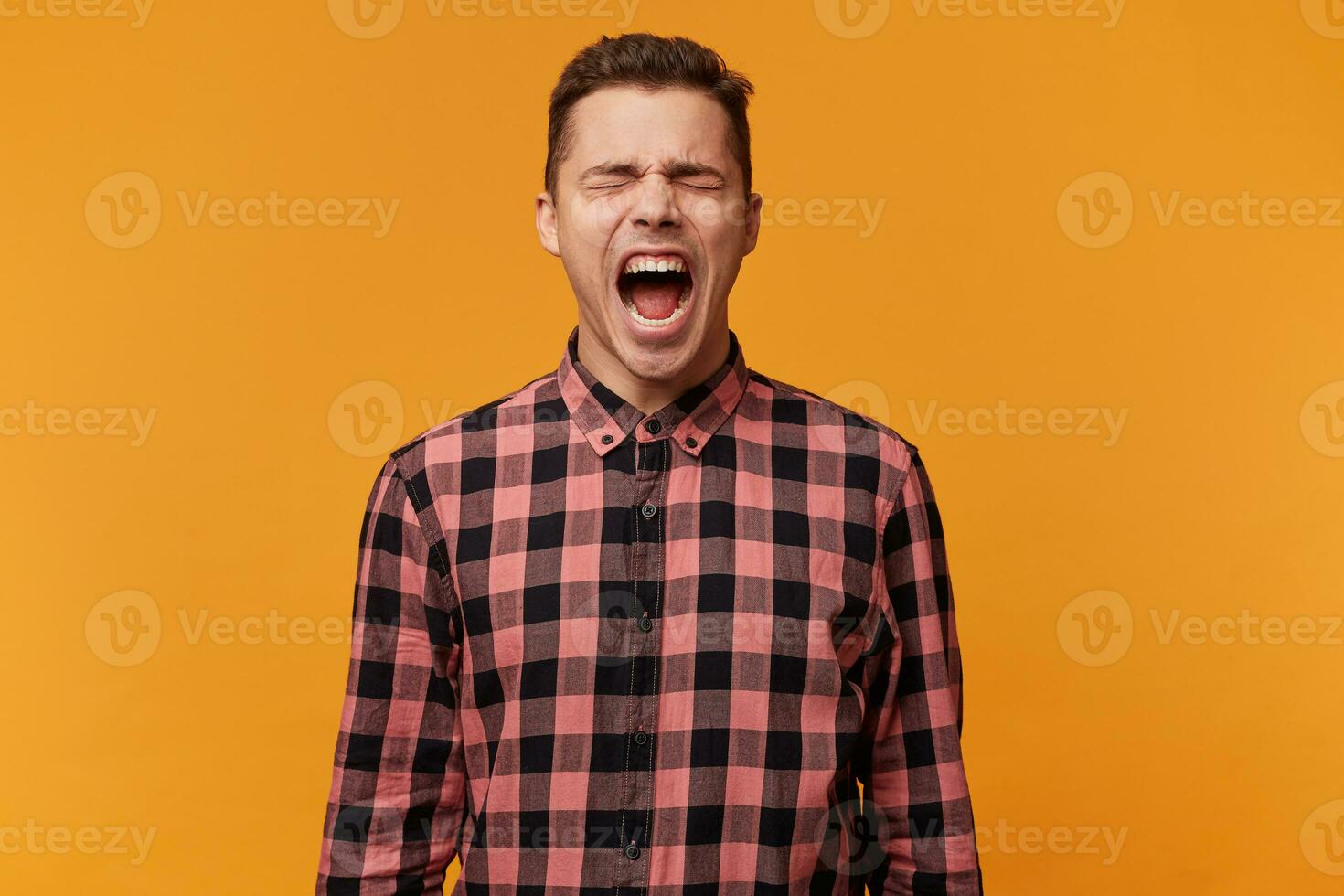 Angry, irate man, with mouth opened in a shout isolated over yellow background. A manager who can no longer restrain his emotions, tired of problems at work went into a separate room and shouted. photo