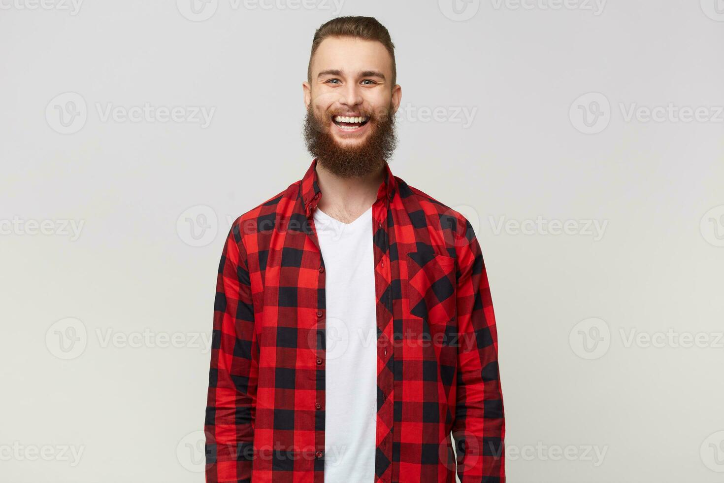 Studio shot of excited funny young attractive bearded man, dressed in shirt, has happy joyful face expression, smiling, laughing isolated on white background photo