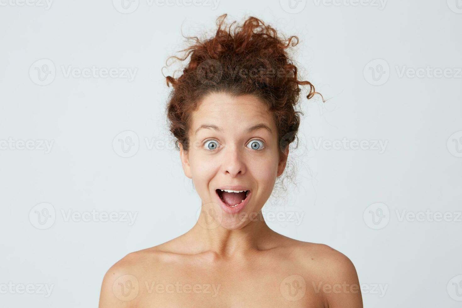 Horizontal shot of surprised pretty young woman with healthy soft skin after applying mask or body cream, curly hair and opened mouth shouting and looks amazed isolated over white wall photo