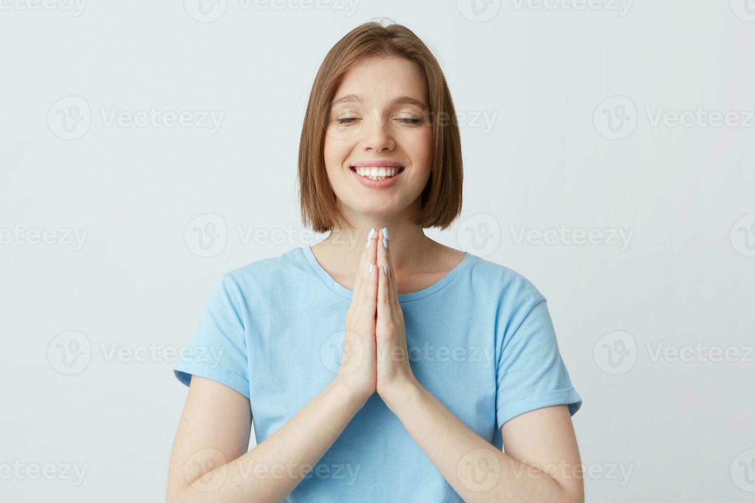 contento pacífico hermosa joven mujer en azul t camisa mantener manos doblada en Orando posición y ojos cerrado aislado terminado blanco antecedentes sonriente y meditando foto