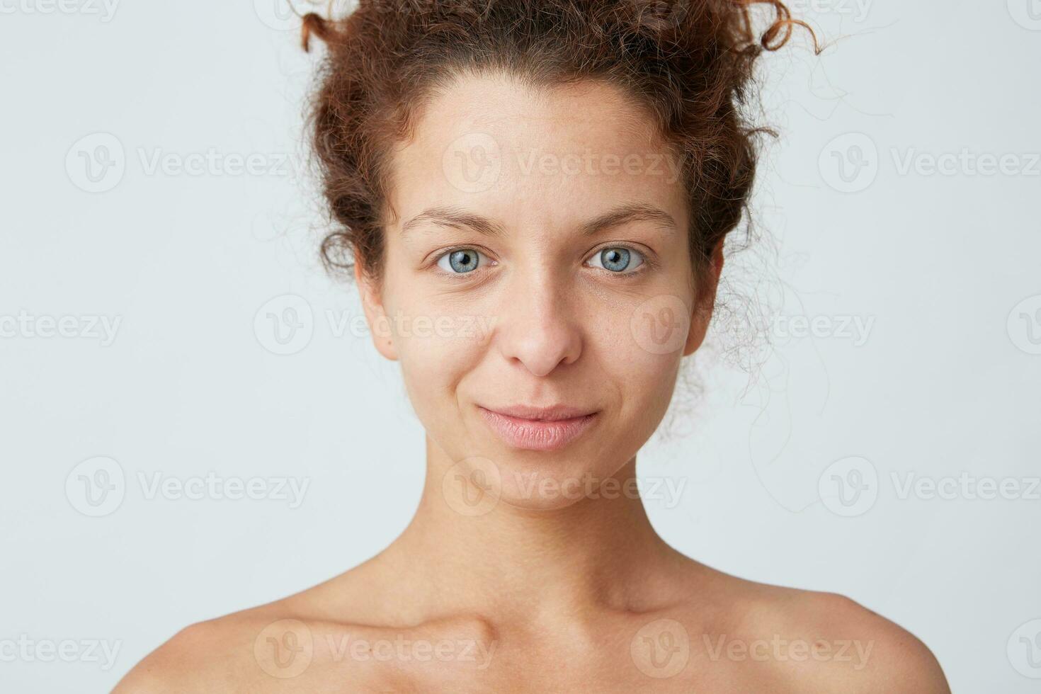 cerca arriba Disparo de atractivo natural joven mujer con Rizado cabello, azul ojos y Perfecto sano piel después ducha y aplicando crema o máscara mira satisfecho aislado terminado blanco antecedentes foto