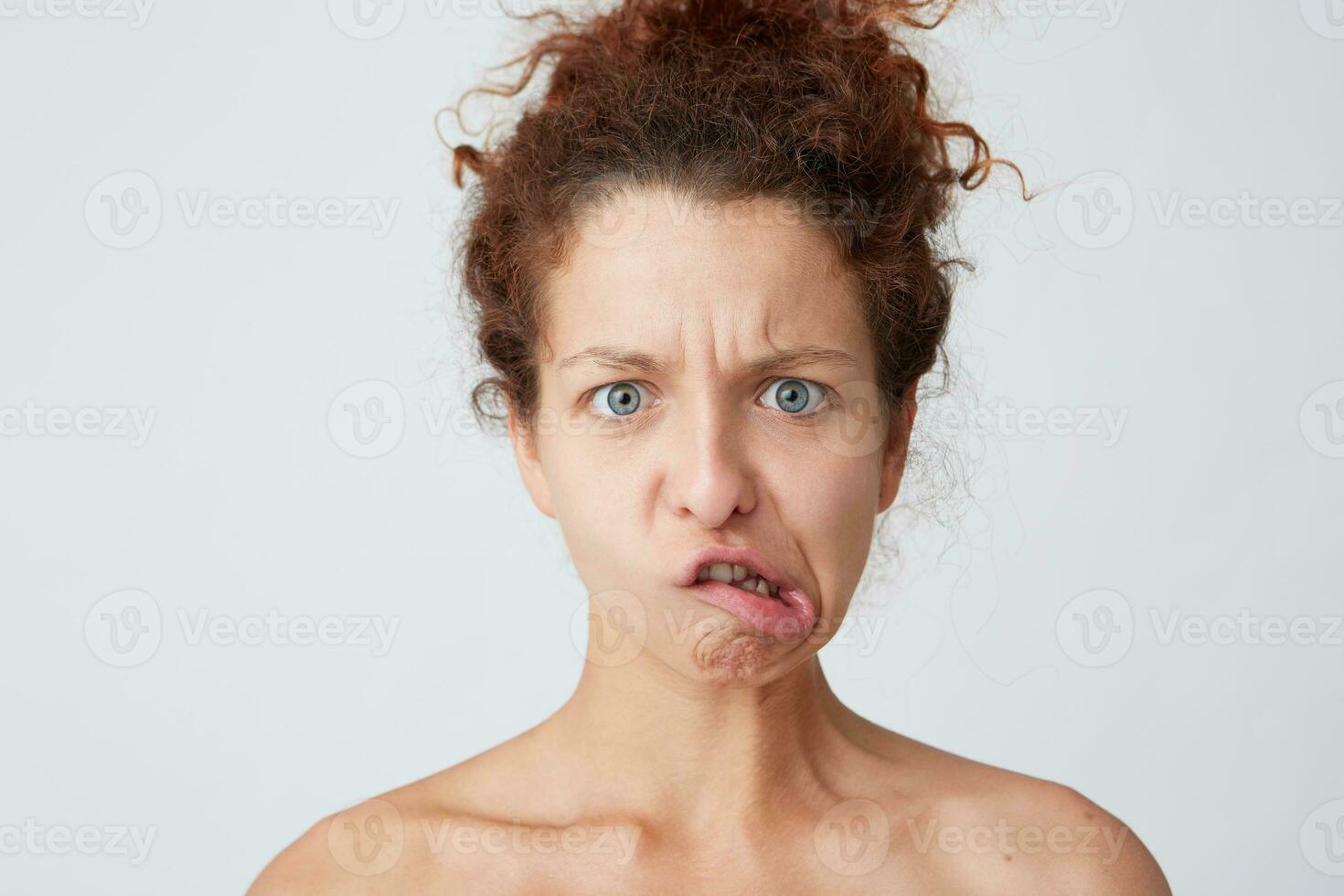 Cropped shot of angry crazy young woman with curly hair and perfect skin after applying mask or cream making irritated funny face and joking isolated over white background Amusing and comical girl photo