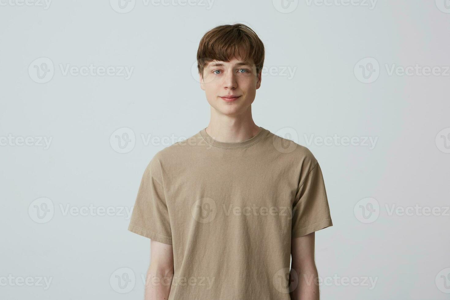 Portrait of handsome attractive young man with short haircut and blue eyes wears beige t shirt standing and smiling isolated over white background Looks directly in camera photo