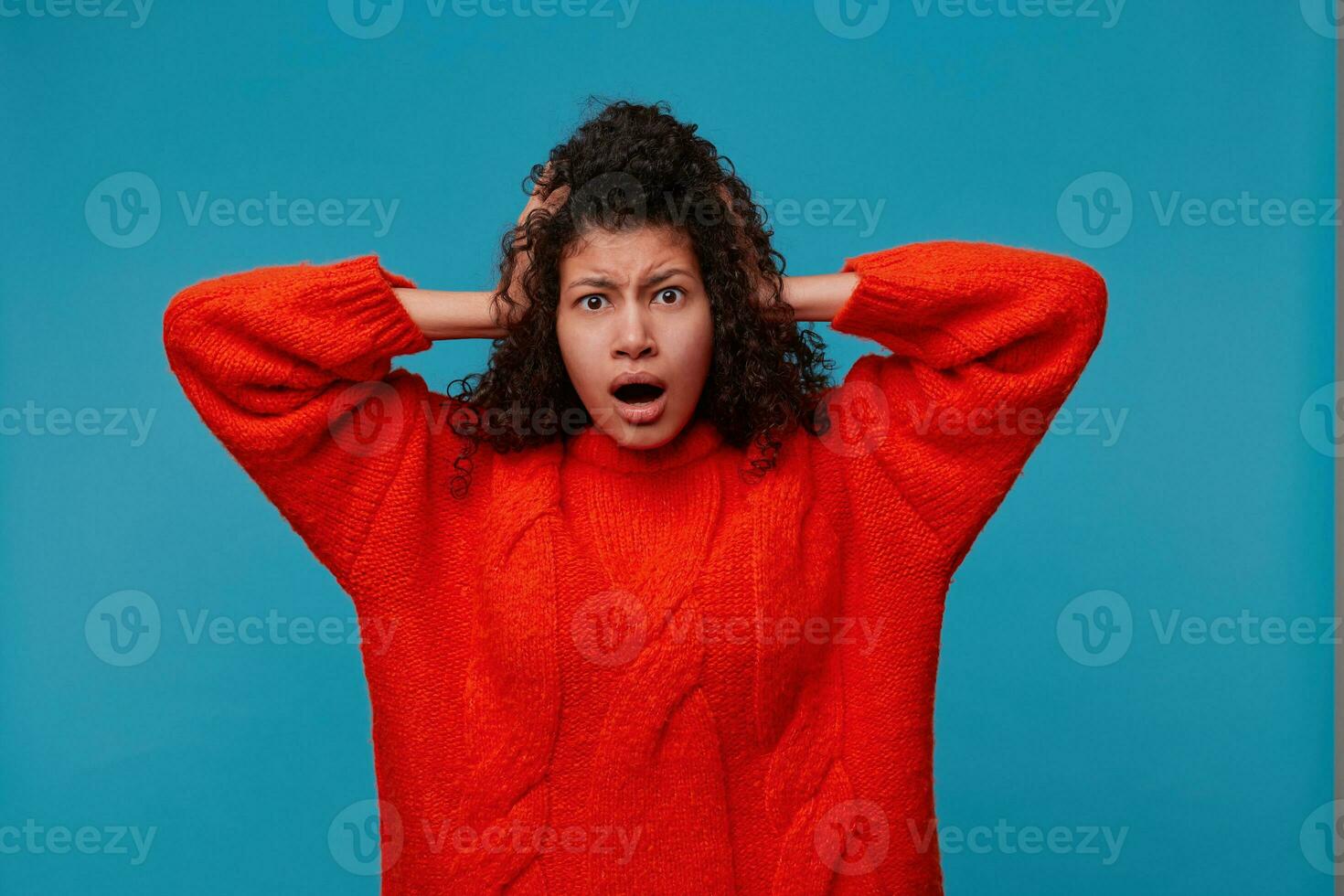 Studio shot of frightened young female feeling scared and shocked, watching horror scene. Attractive dark-skinned woman dressed casually having terrified look while receiving shocking news photo