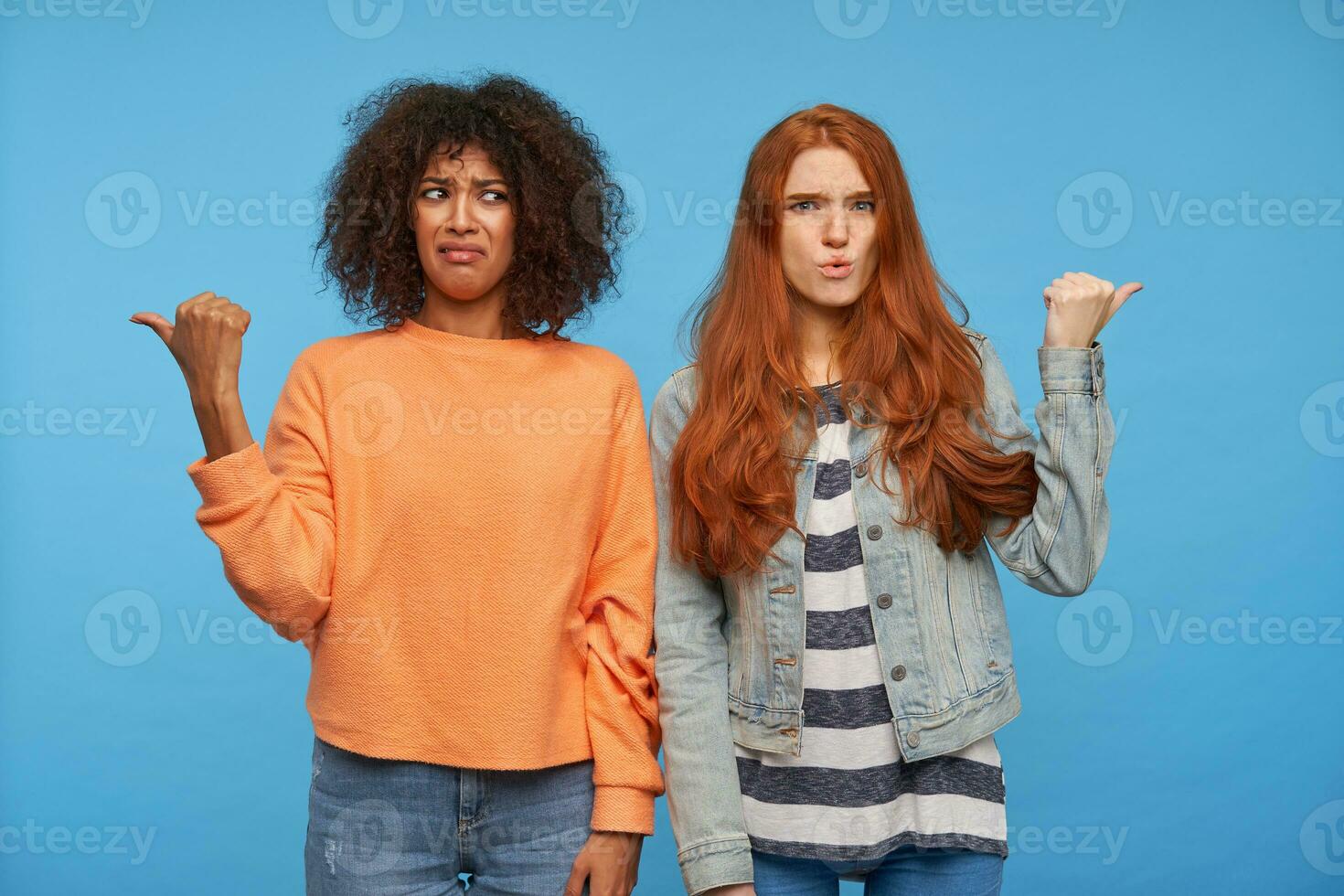 Confused young attractive women frowning their eyebrows with pout and showing in different directions with raised hands, isolated over blue background photo