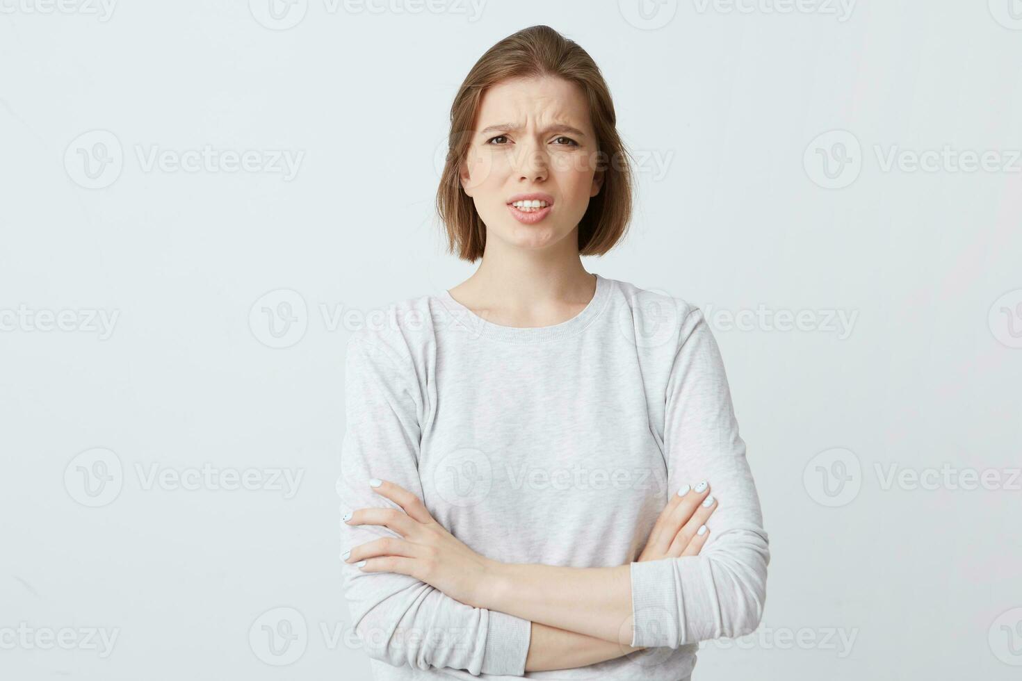 Closeup of angry annoyed young woman in long-sleeve standing with arms crossed and feels irritated isolated over white background Looks directly in camera photo