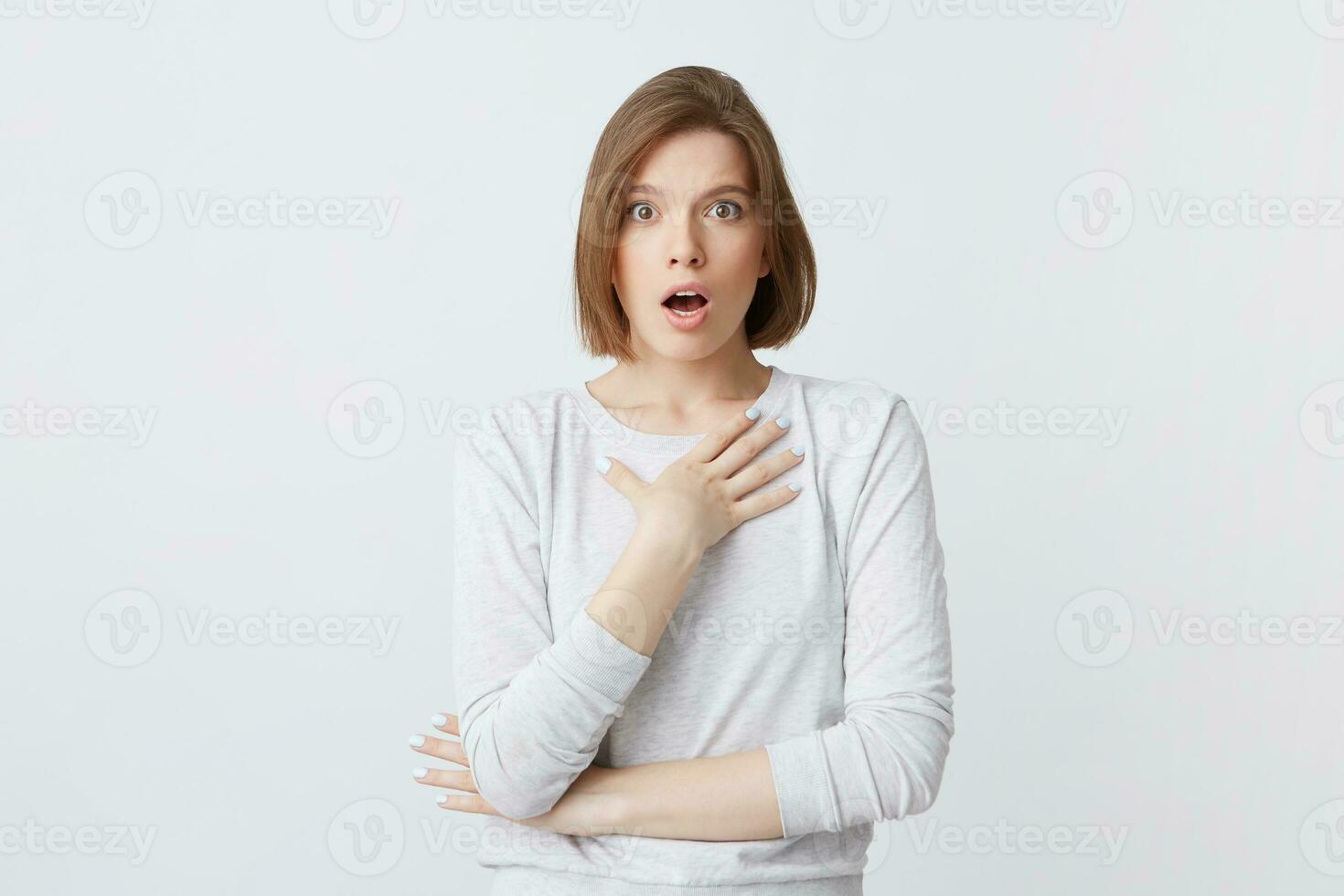 Amazed lovely young woman in long-sleeve standing with opened mouth and hands folded isolated over white background Feels shocked photo