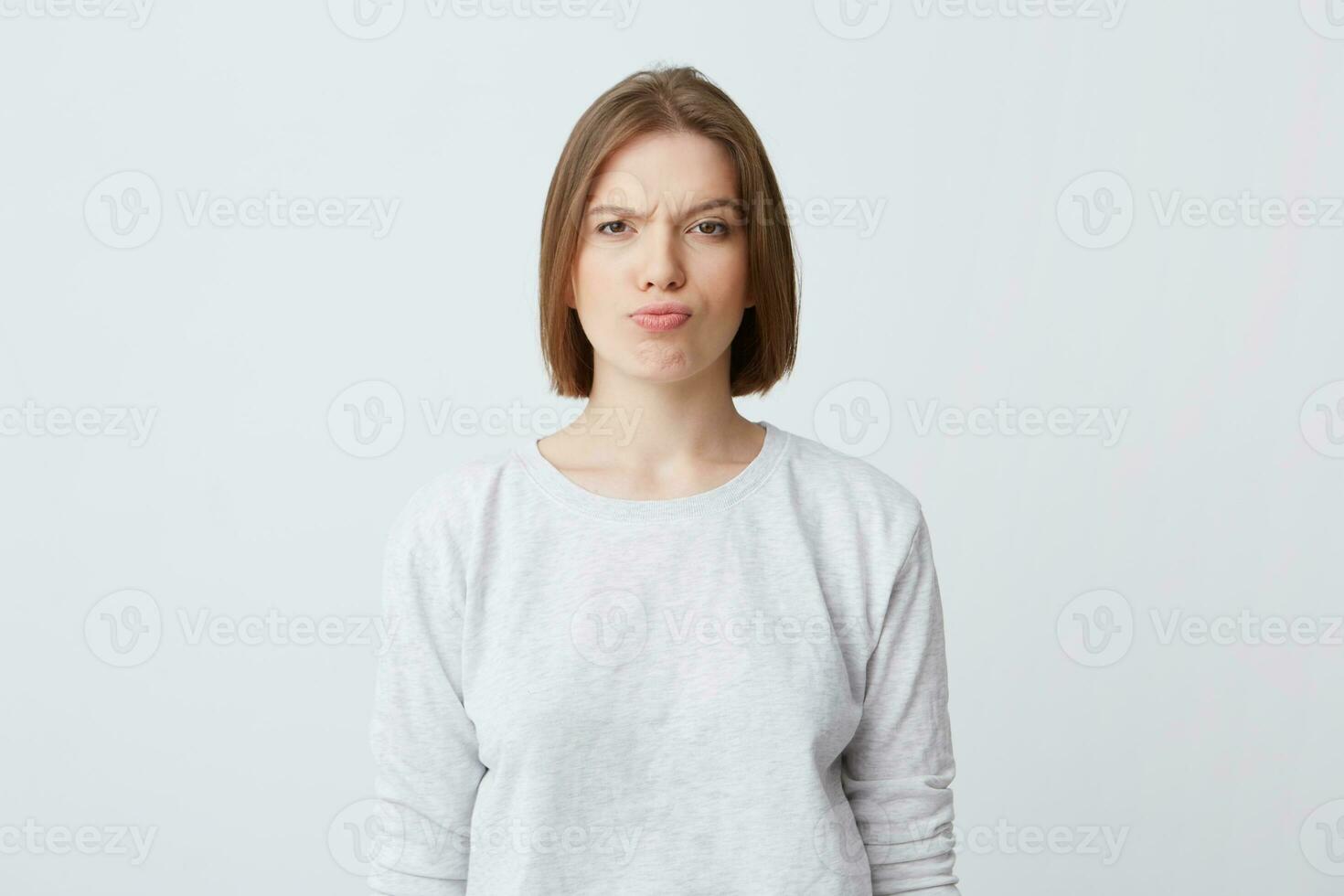 Portrait of serious unhappy young woman in long-sleeve standing and frowning her face isolated over white background Looking directly in camera photo