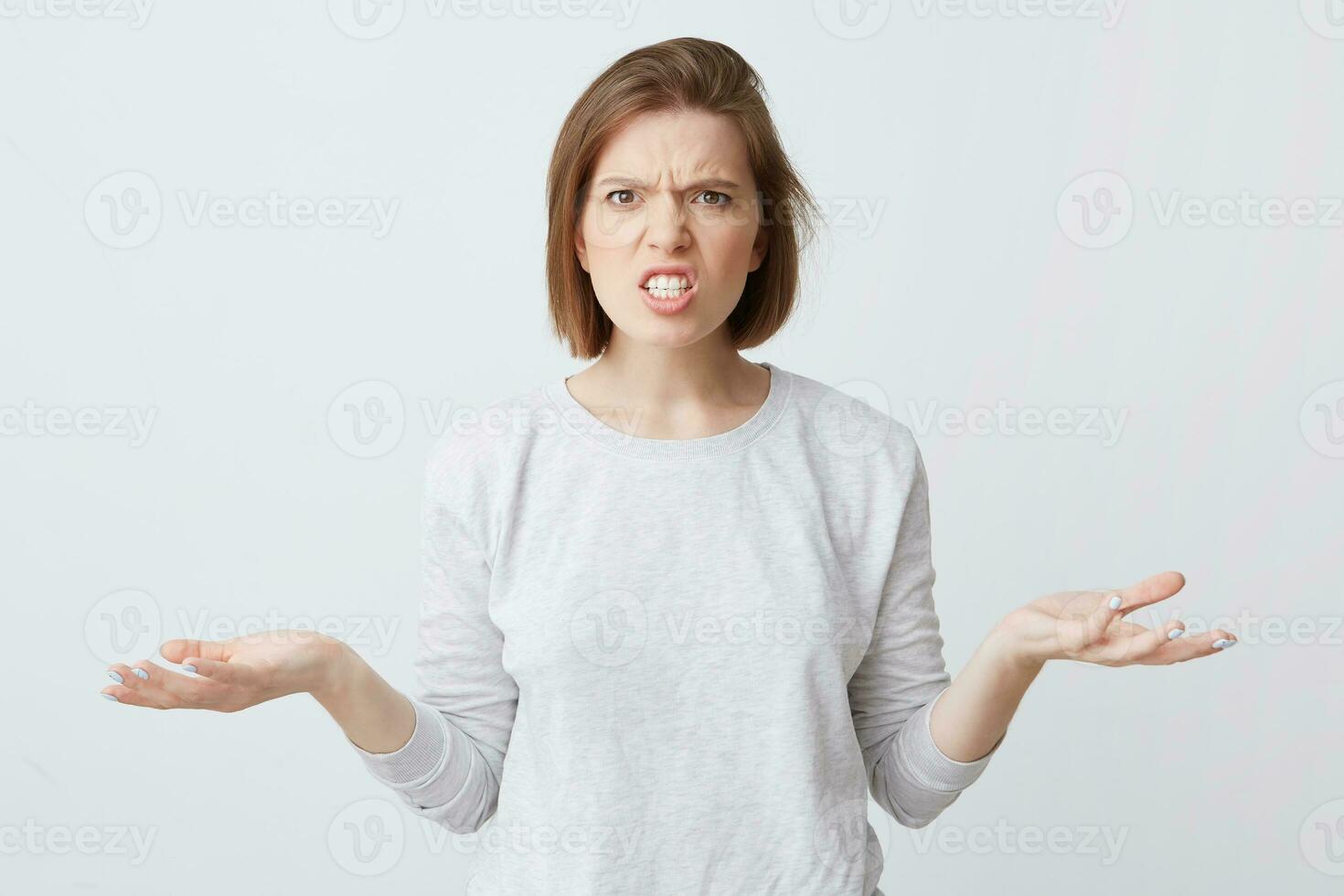 Portrait of mad irritated young woman in long-sleeve feels angry and holding copy space on both palms isolated over white background photo