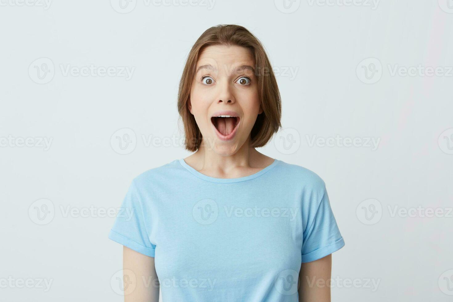 Portrait of surprised happy young woman with opened mouth in blue t shirt feels excited and shouting isolated over white background photo